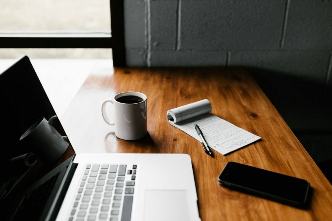 A laptop, coffee and notebook on a wooden desk