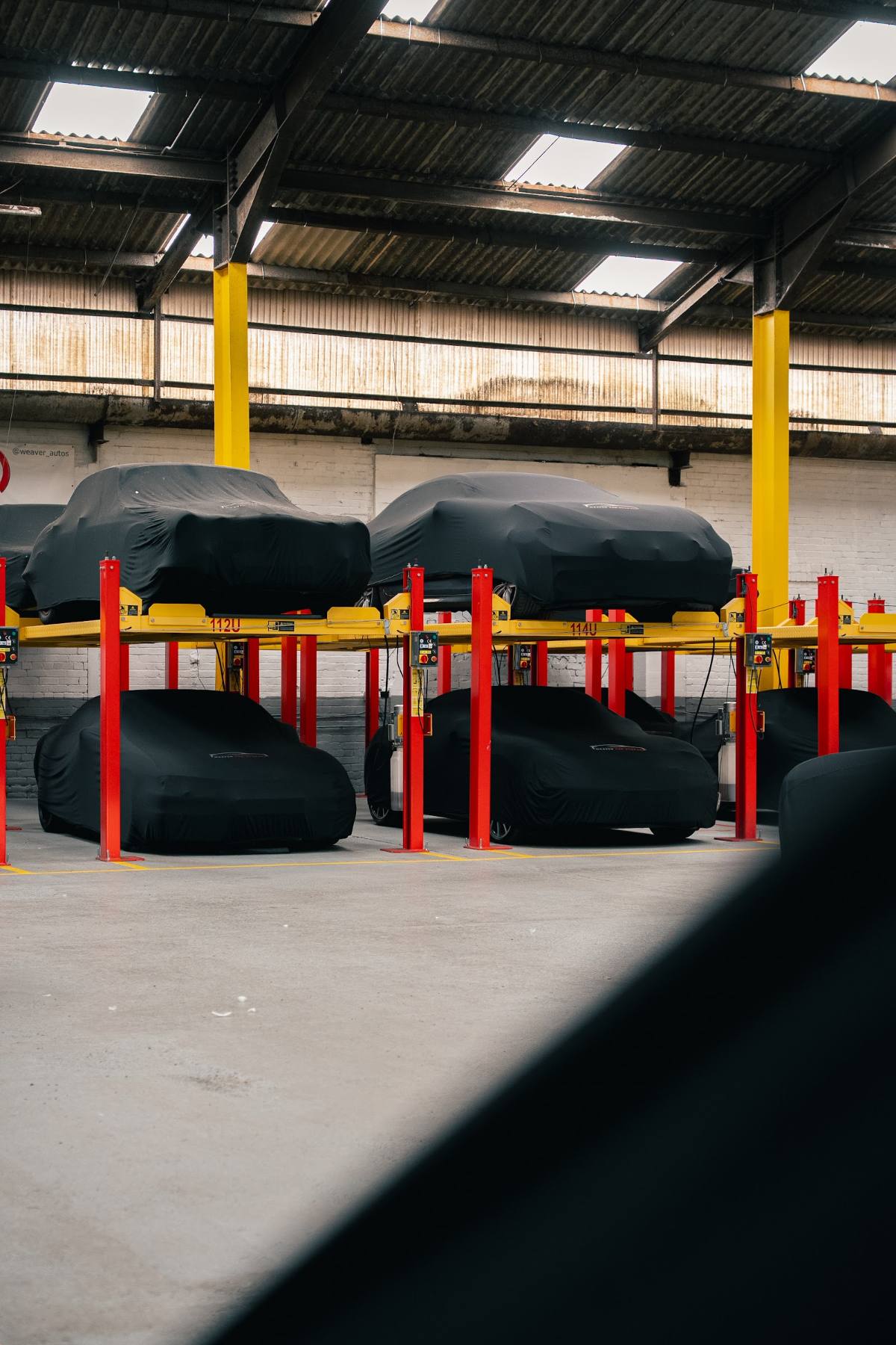 Covered cars stacked on red and yellow lifts